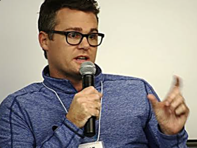 William Skelley speaking into a microphone at an event